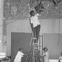 The TV studio is being prepared for a shooting session. Notice the presenter standing before a map of India which still needs to be raised in position next to her.