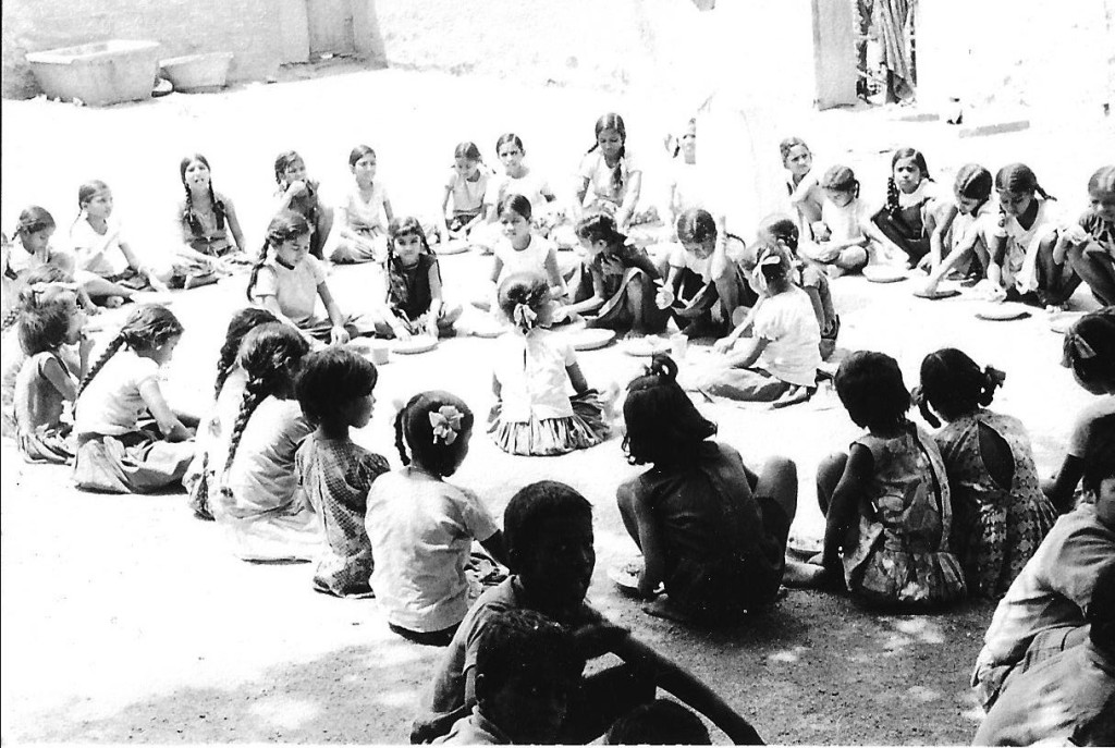 Girls in a boarding school having their main meal: rise, curry and dhal on tin plates.